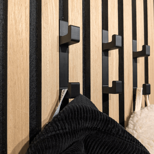 Schwarze 3D-gedruckte PLA-Haken für eine DIY Garderobe an Akustikpaneelen. Gezeigt mit einer Jacke und Accessoires, stabil montiert ohne Bohren.