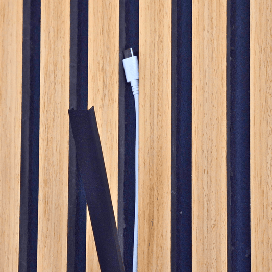 Kabelchaos an der Akustikpaneel-Wand: Ein herabhängendes USB-C Ladekabel vor der Montage der schwarzen Kabelabdeckung. Unordentliche Kabel stören das Design der Holzlamellenwand.