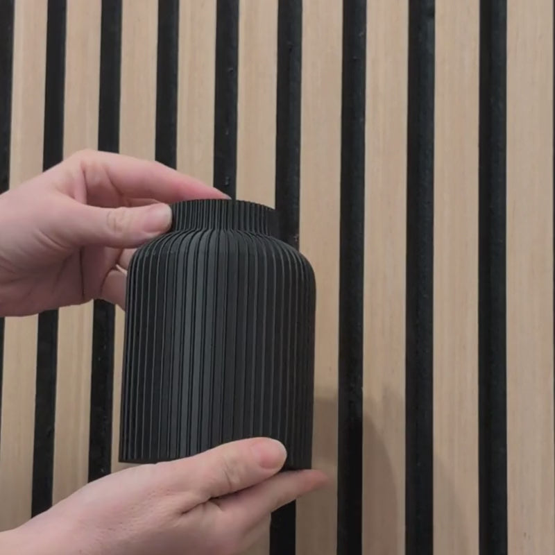Video-Anleitung: Montage der schwarzen Wandvase am Akustikpaneel in 15 Sekunden. Gezeigt wird das einfache Einstecken und 90-Grad-Drehen in die Holzlamellen ohne Bohren oder Kleben – minimalistische Dekoration von Mondhäuschen.