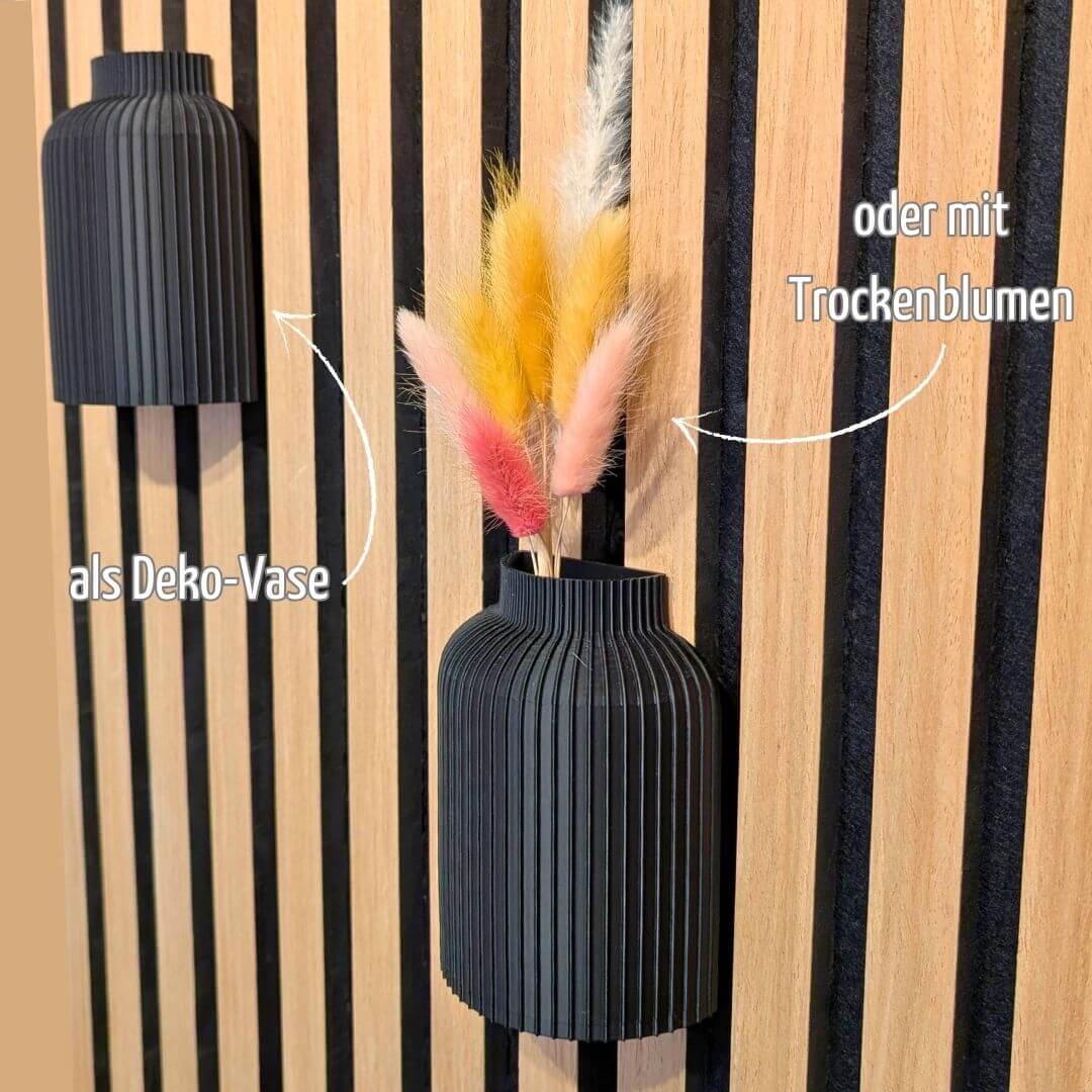Infografik zeigt zwei schwarze 3D-Druck Wandvasen auf einem Akustikpaneel: Eine links als schlichte Deko-Vase und eine mittig mit bunten Trockenblumen dekoriert. Text-Hinweis auf vielseitige Nutzung ohne Bohren – Mondhäuschen.