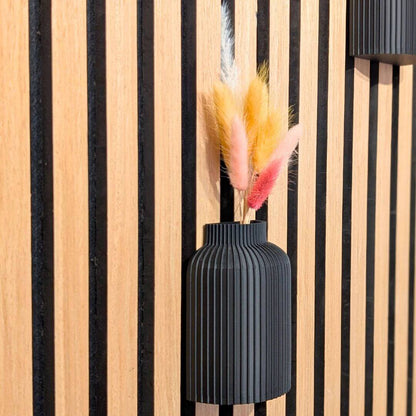 Nahaufnahme einer schwarzen Vase für Akustikpaneele mit bunten Trockengräsern. Fokus auf das minimalistische Design und die einfache Anbringung ohne Werkzeug.
