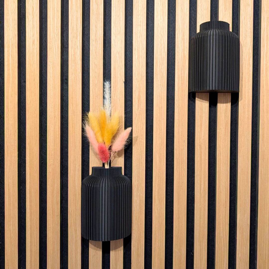 Zwei schwarze Wandvasen für Akustikpaneele in unterschiedlichen Höhen montiert, eine als reines Deko-Objekt und eine mit Frühlings-Trockenblumen.